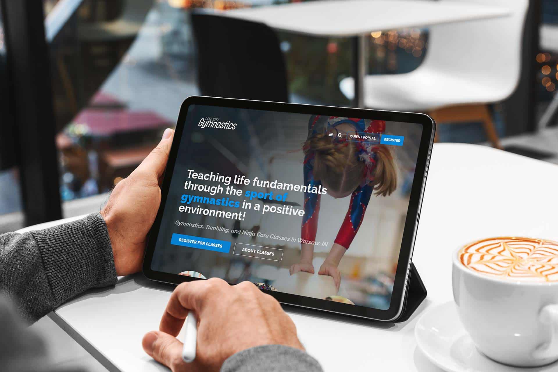 Person viewing Lake City Gymnastics website on a tablet in a café.