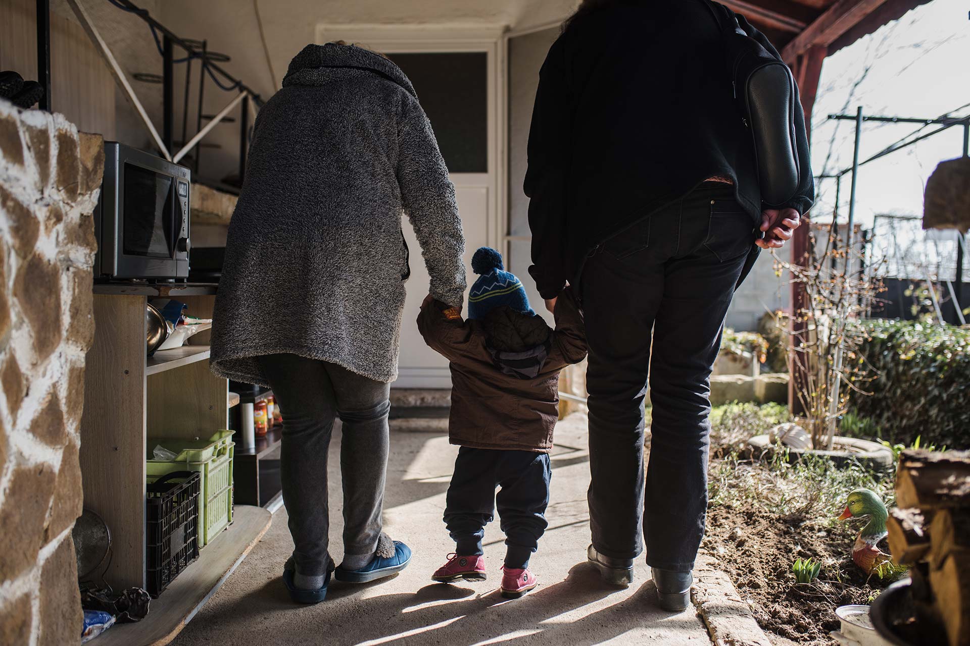 Two adults and a child, hand in hand, on a porch walkway with lost sparrows.
