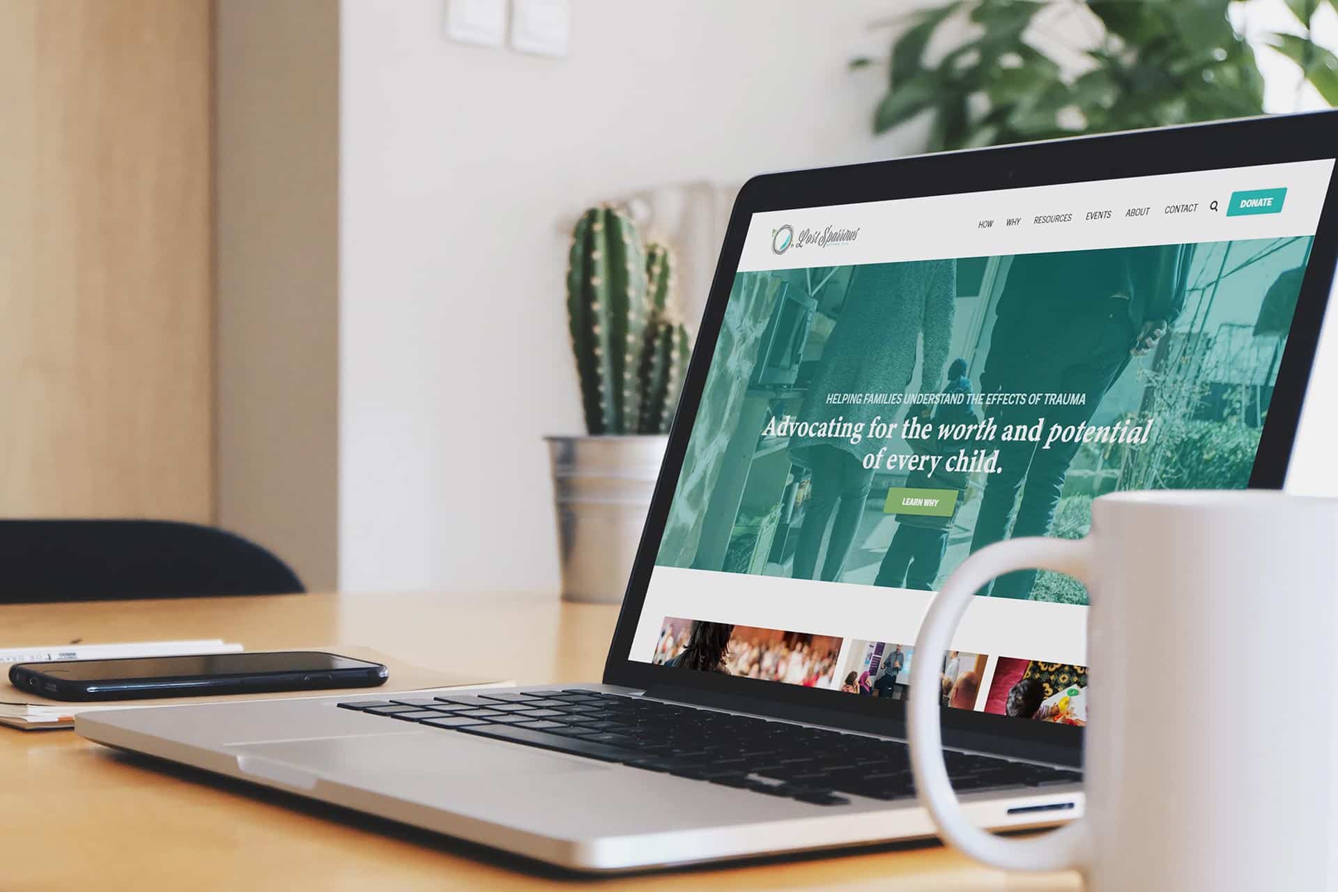 Lost sparrows illustration on laptop, cactus and mug nearby.