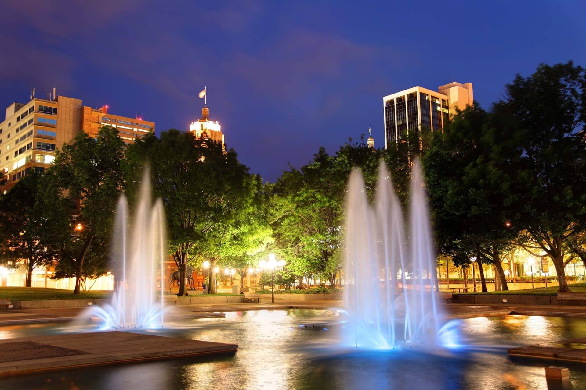 Love Fort Wayne: Fountains glow blue against city towers at night.