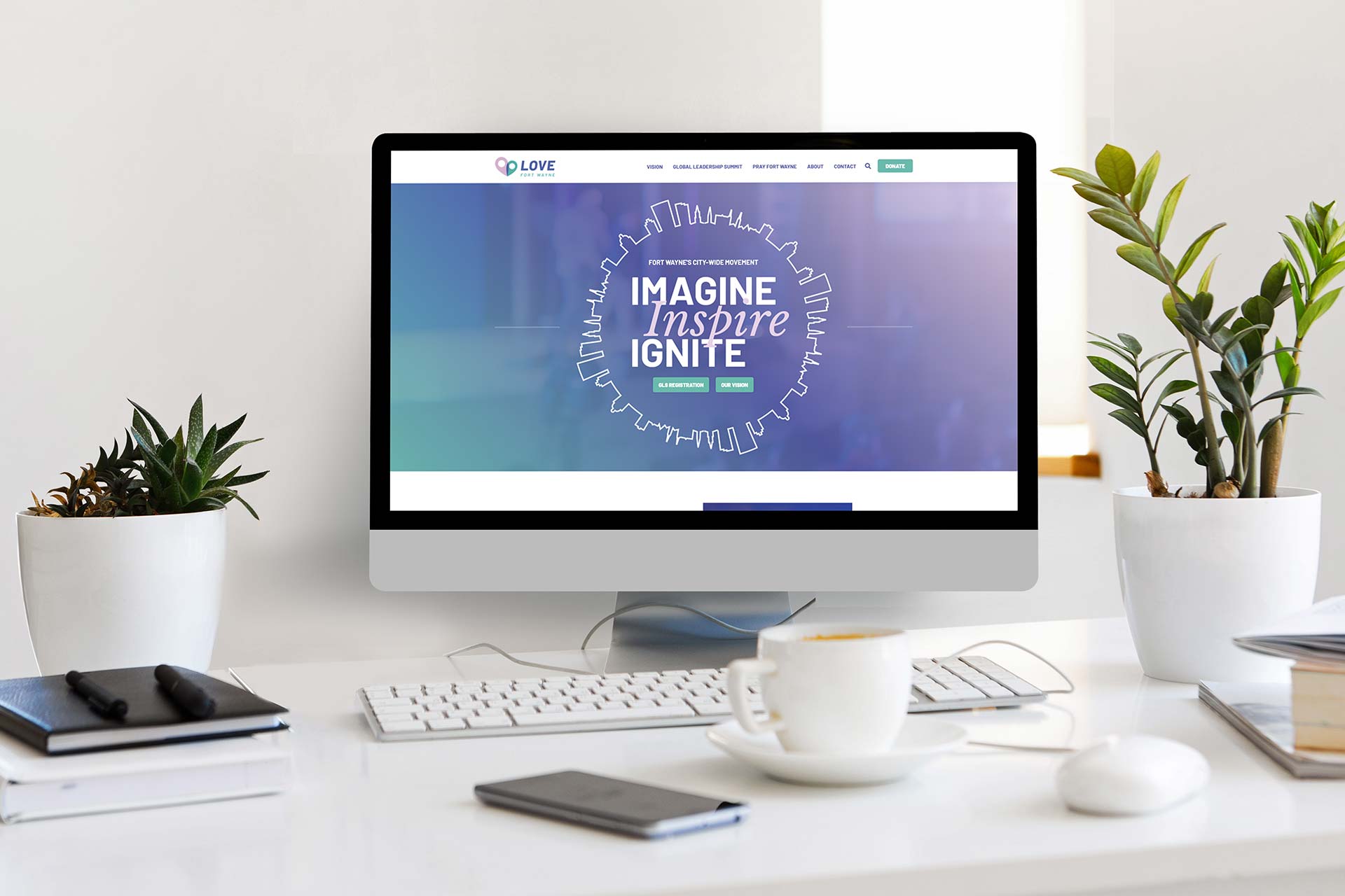 Computer on desk with Love Fort Wayne site, plants, and coffee cup.