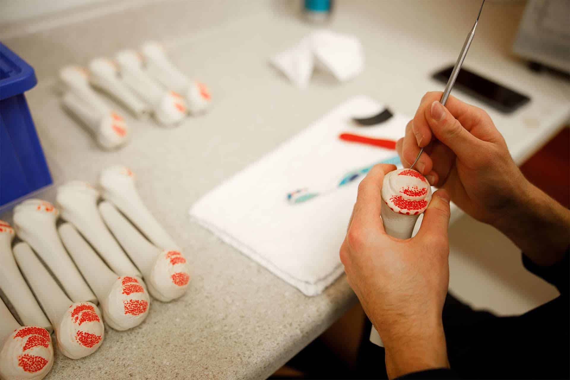 Person painting OsteoShape designs on ceramic handles at a workspace.