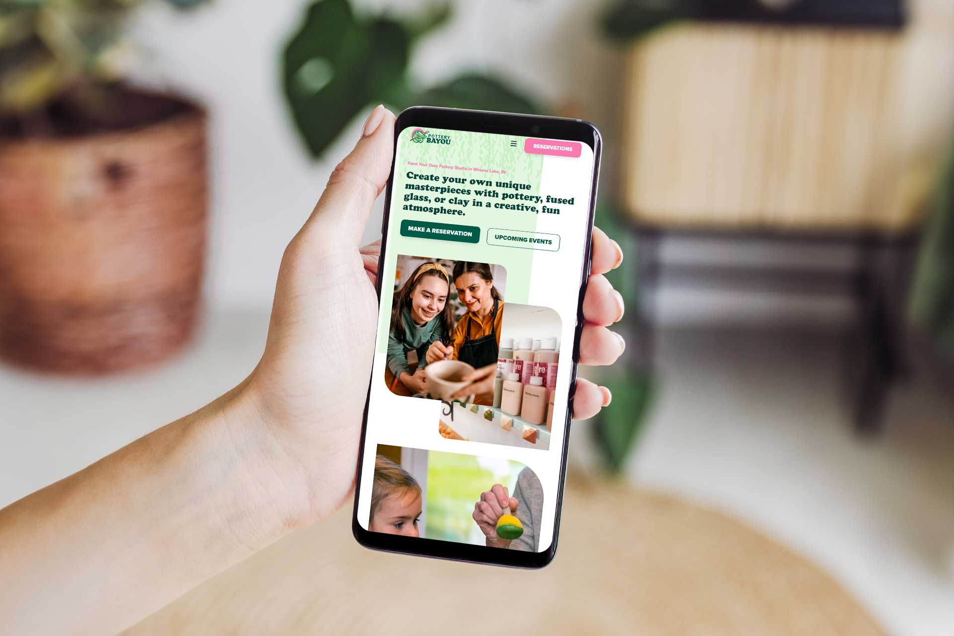 Hand holding smartphone showing Pottery Bayous site on pottery painting.