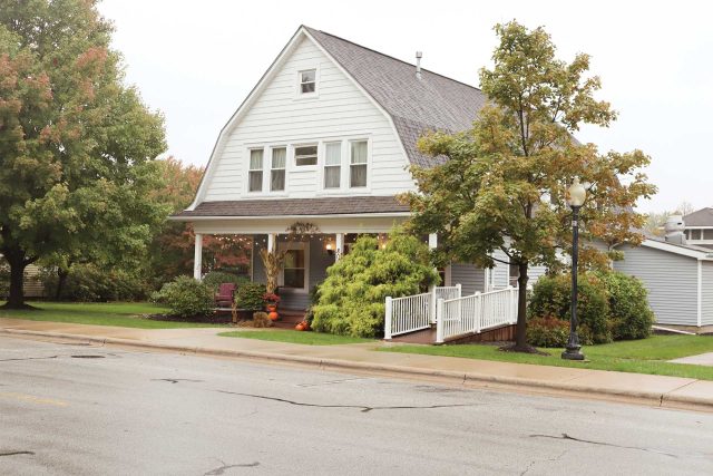 Two-story white house by Pottery Bayou, featuring a porch and ramp, tree-lined.