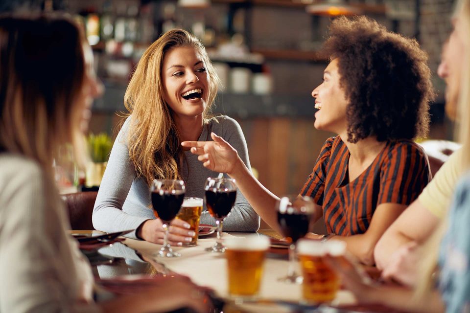 People laughing and chatting at a table with drinks in a restaurant.