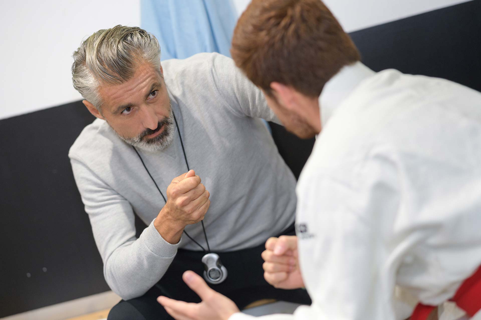 Coach guiding athlete, gestures fluid like a shepherd, stopwatch around neck.