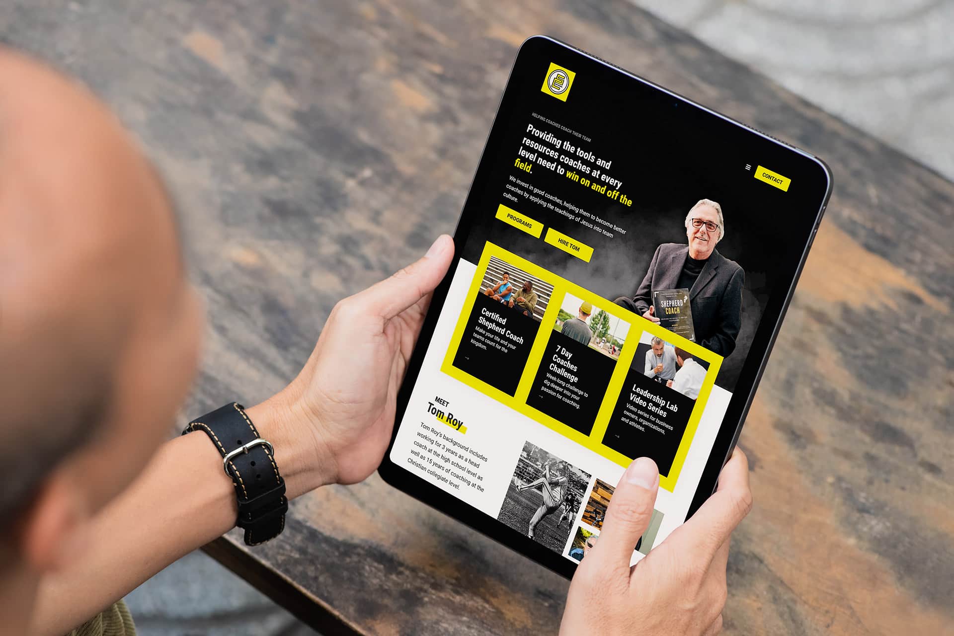 Person holding a tablet showing the Shepherd Coach Network site with vibrant images.