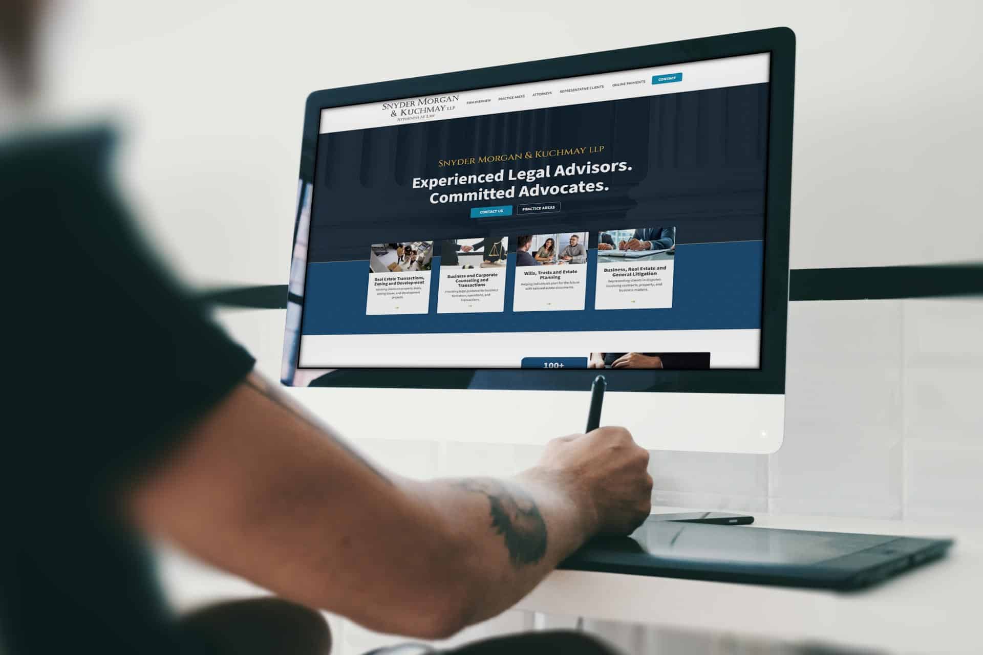 Person using a digital pen at a desk with a legal firms website on a monitor.