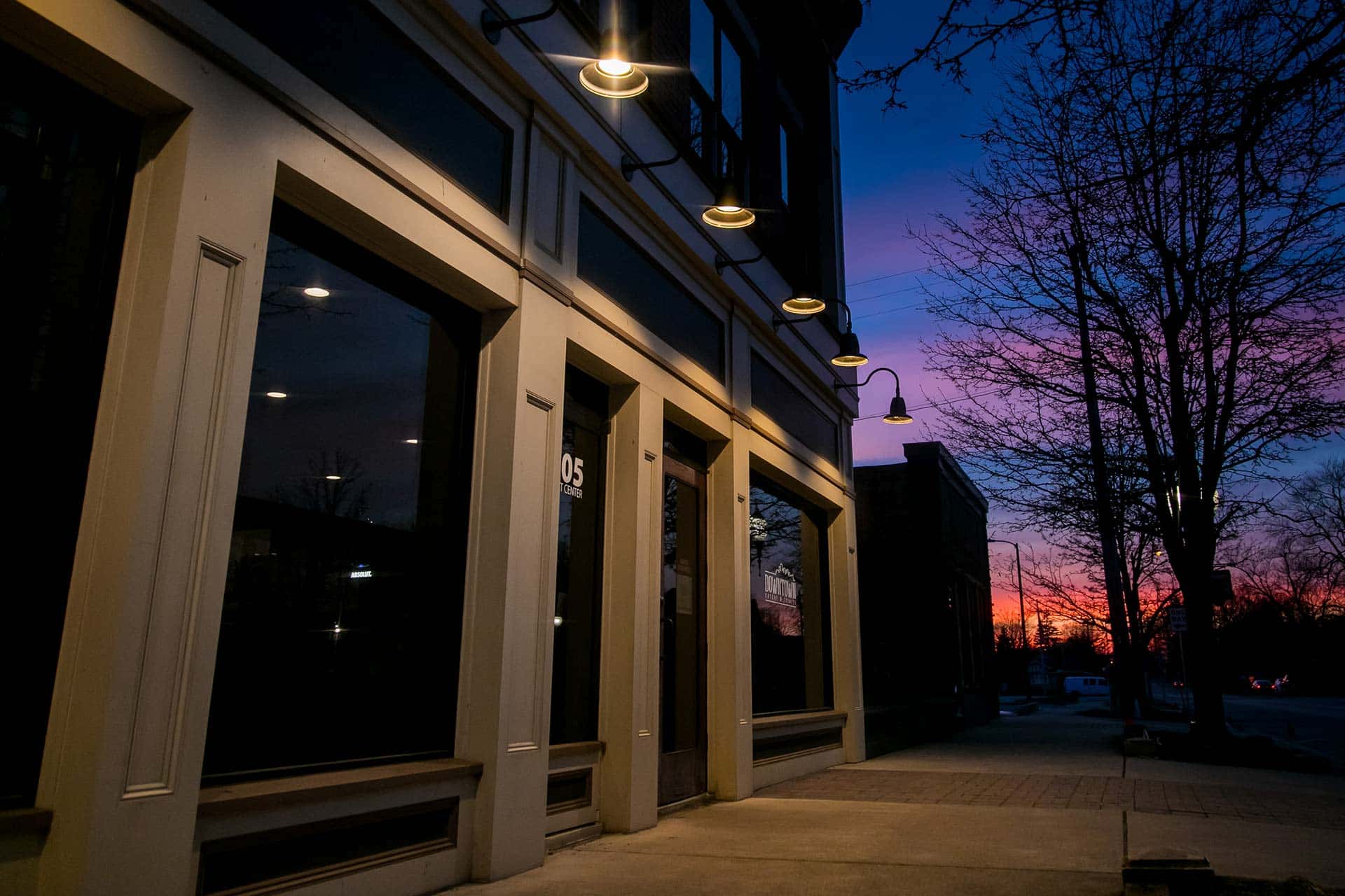 Building exterior at dusk with lit street lamps and a colorful sunset.