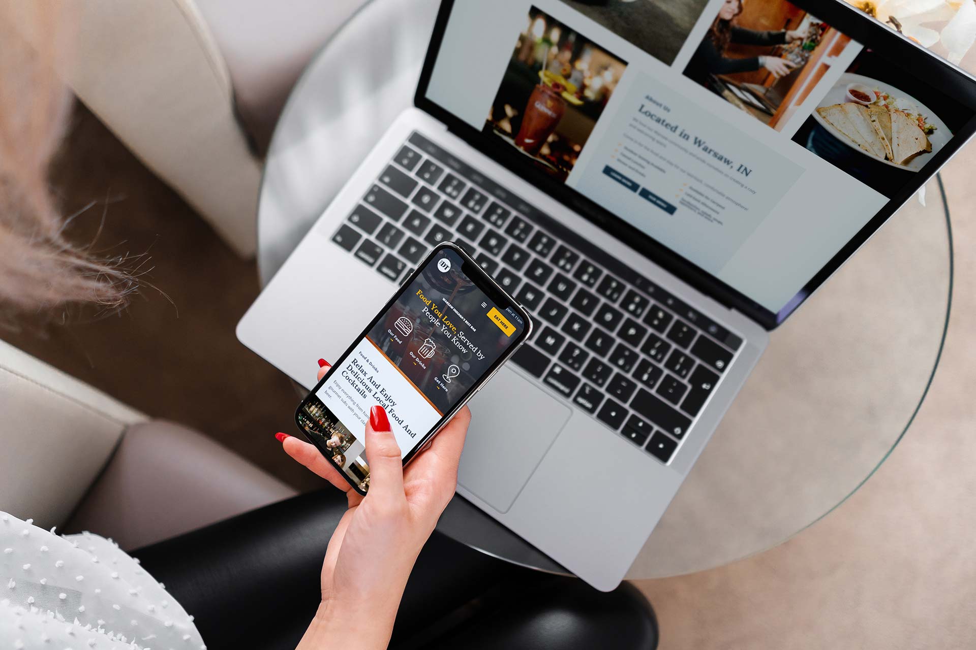 Person using a smartphone while a laptop is open on a glass table.