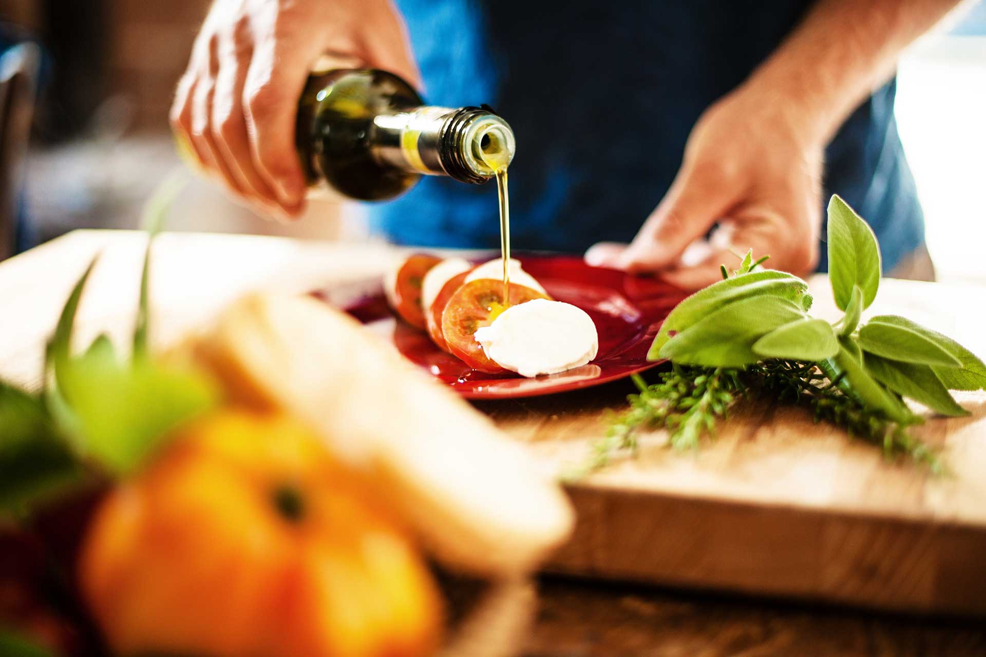 Person drizzling olive oil over sliced tomatoes and mozzarella on a plate.