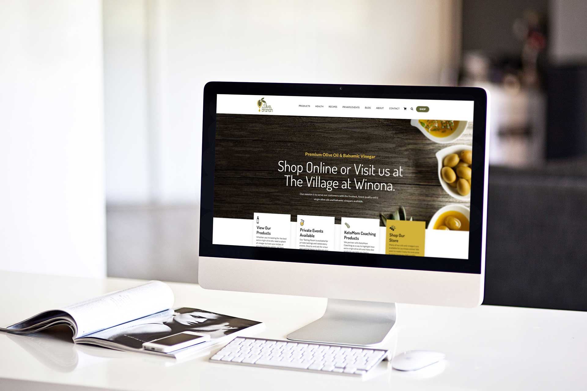 Computer displaying a website for a shop, on a white desk with magazines.