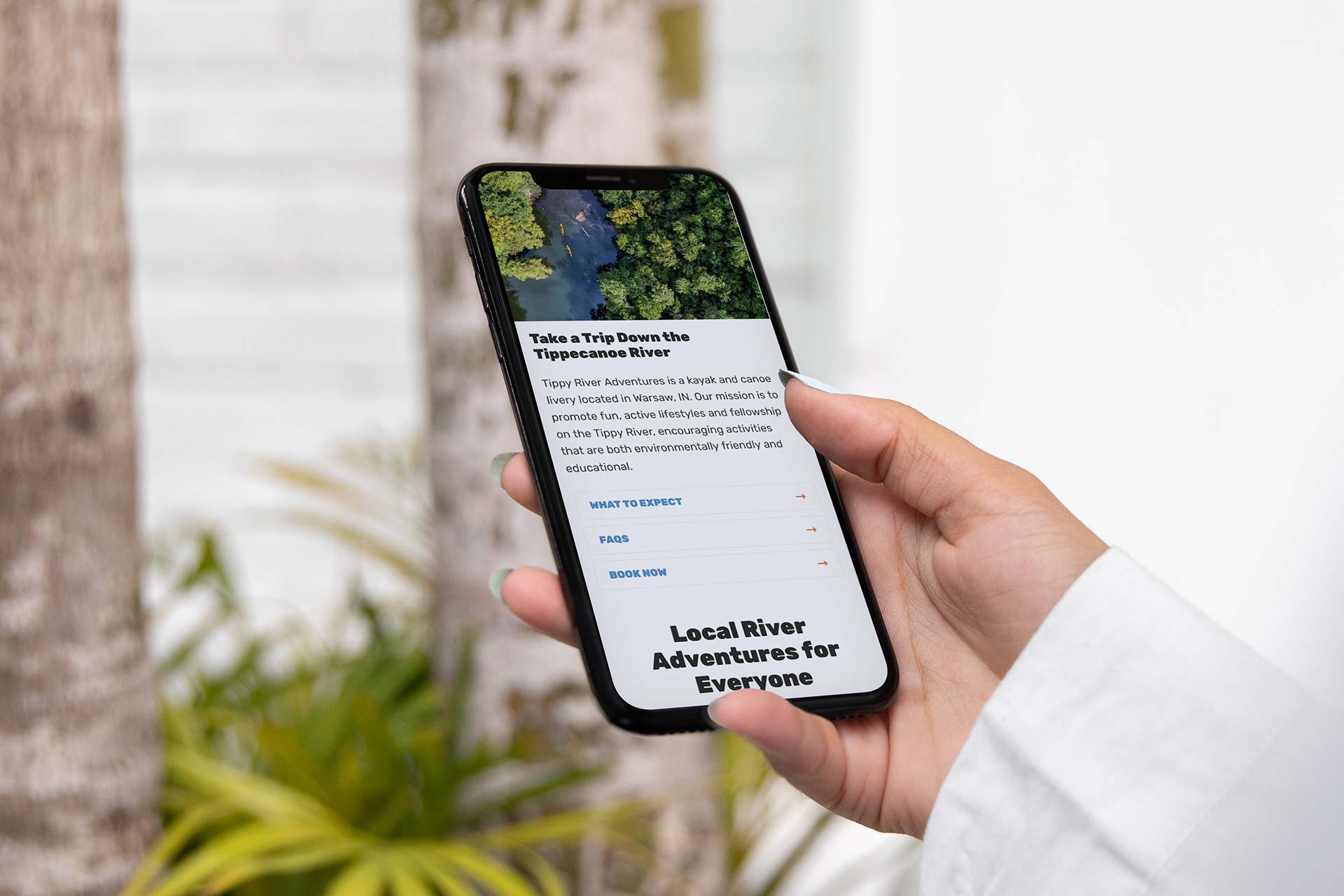 Person holding a phone displaying the Tippy River Adventures website.