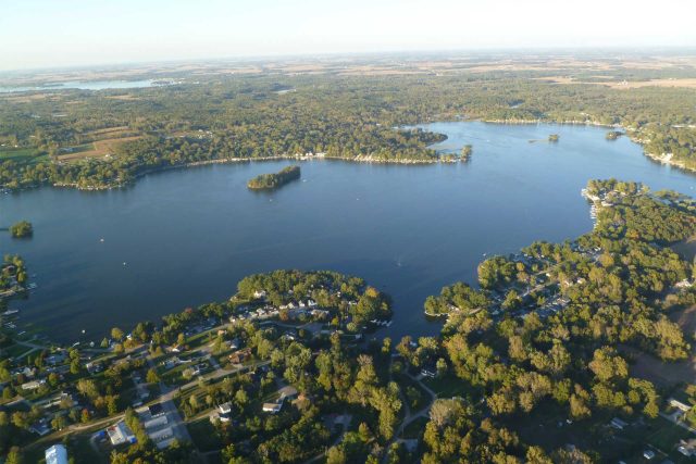 Aerial view of The Watershed Foundations lake with trees and homes nearby.