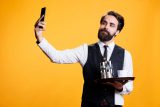 Man in formal attire takes selfie with tray for website content backdrop.
